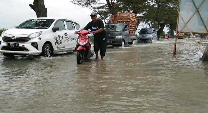 MOGOK. Pengguna jalan sedang mendorong motornya, karena memaksa melewati jalan yang masih terendam banjir.